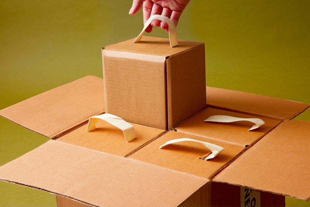 hand using cotton strap to pull cardboard box out of larger cardboard box