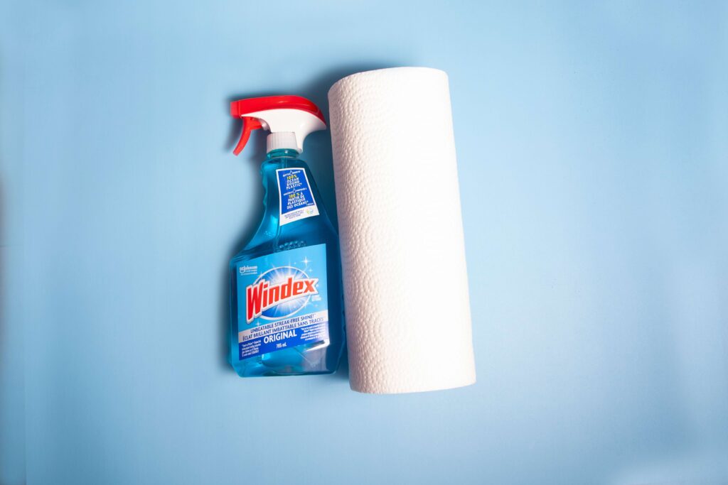 spray bottle of windex and roll of paper towels on blue background