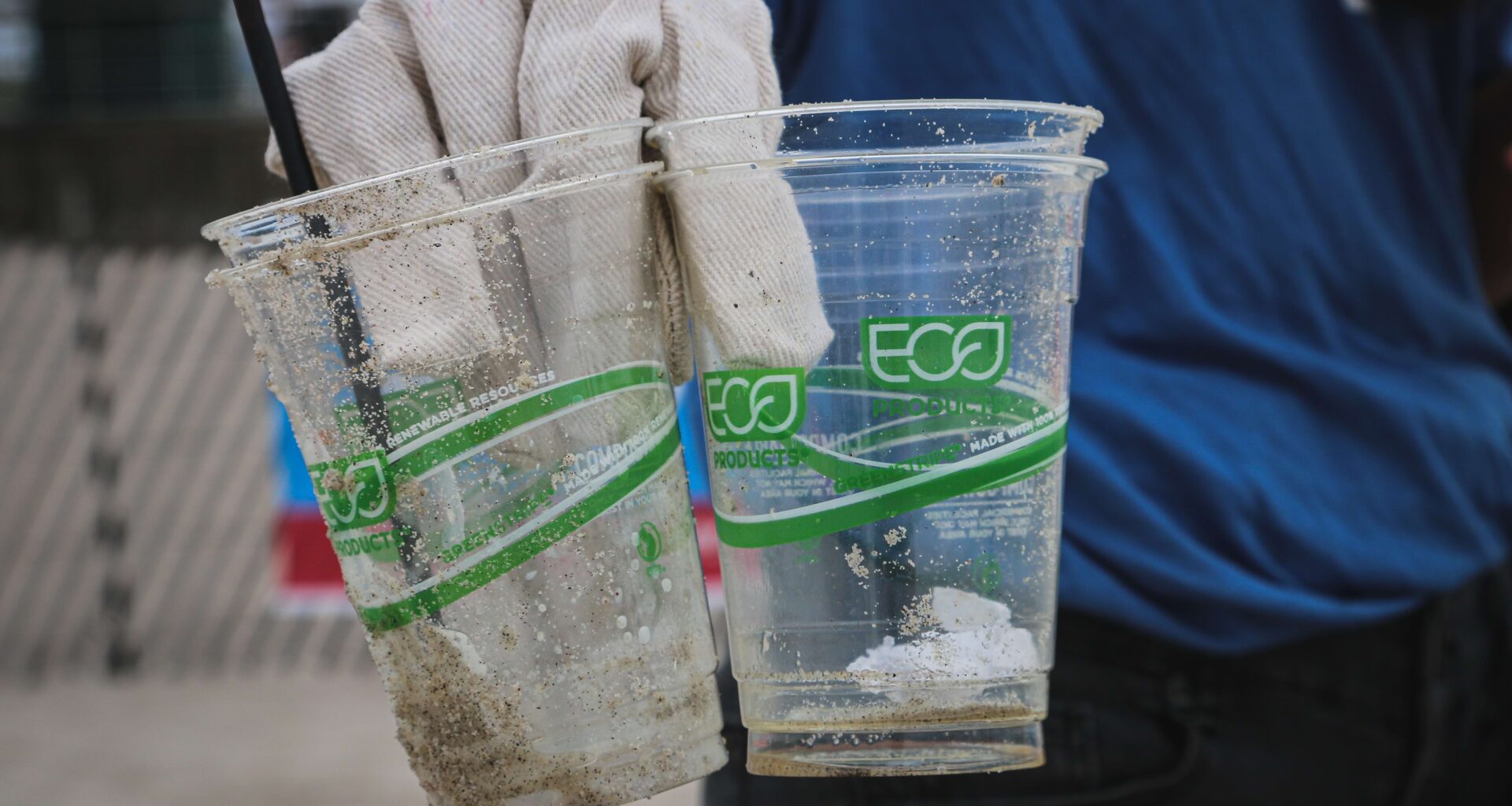 gloved hand holding two dirty biodegradeable plastic cups