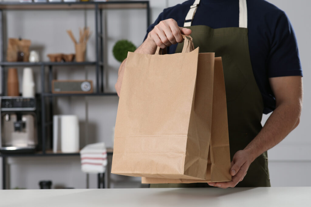 a restaurant employee holding a Kraft paper bag containing food.