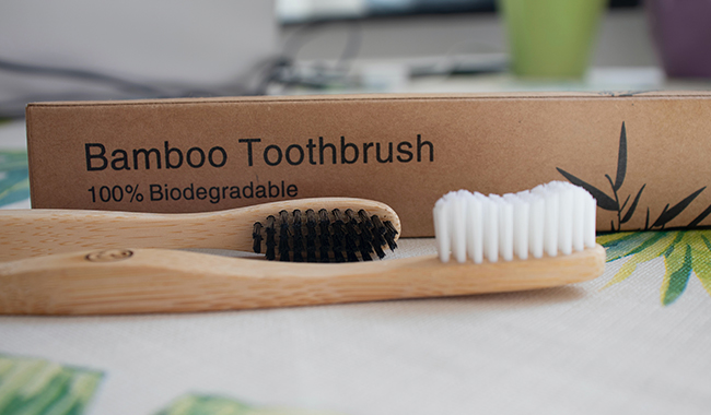 Bamboo toothbrush with charcoal bristles beside its sustainable dental packaging